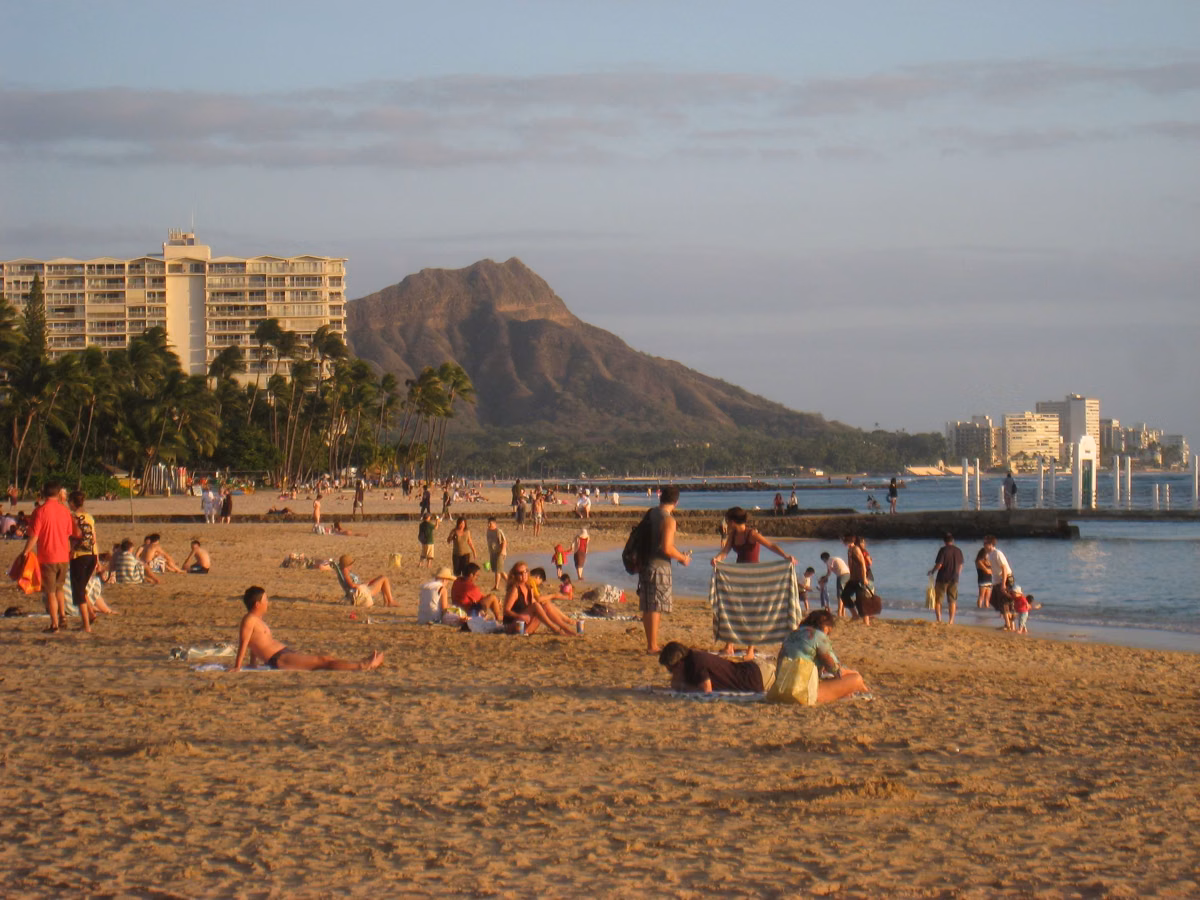 Beachgoers on the sand at Waikīkī in late afternoon light, with Diamond Head beyond