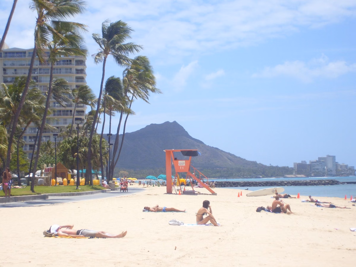 Diamond Head behind palm trees and a lifeguard tower on Waikīkī Beach