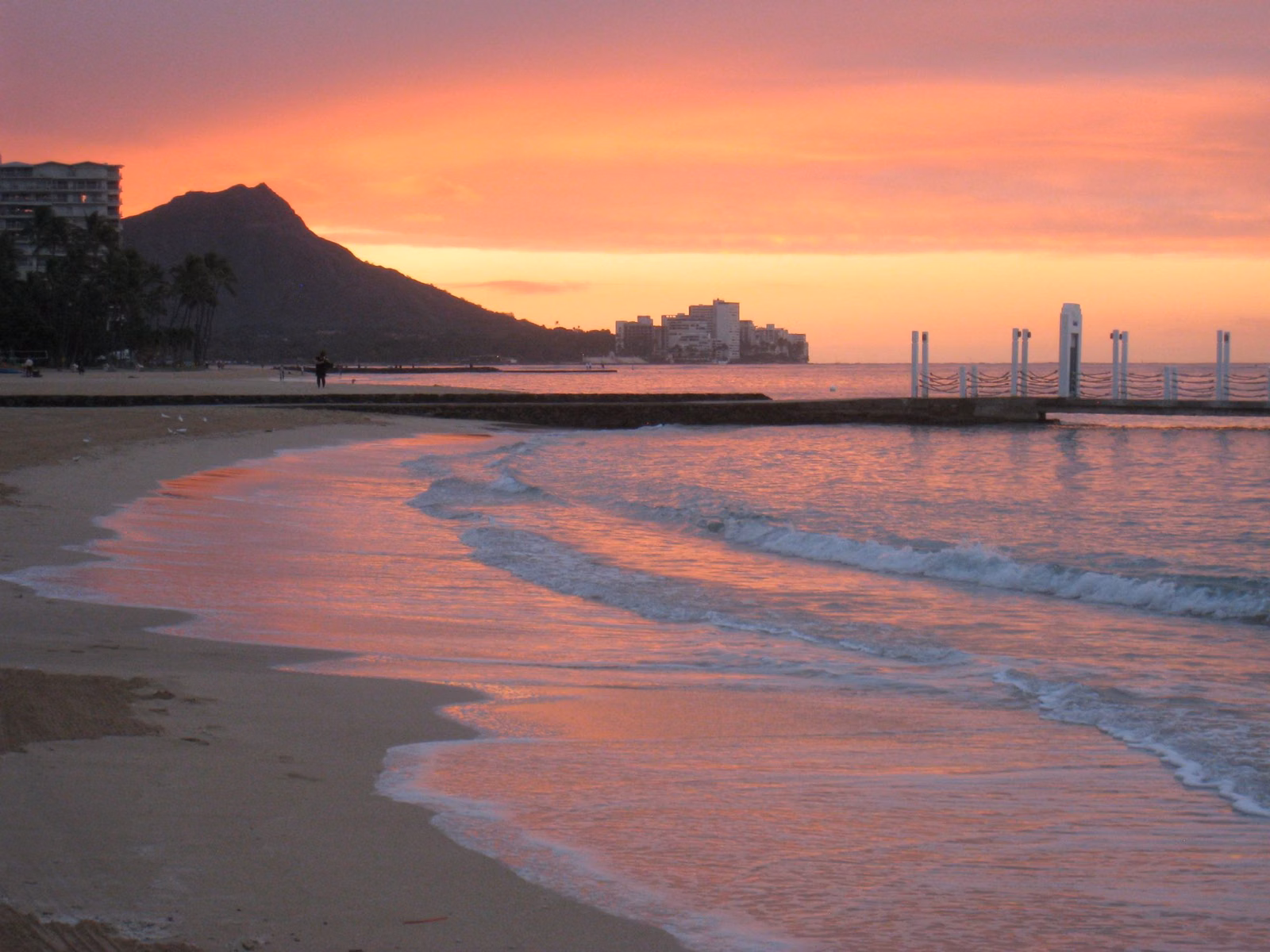 Waves washing up a Waikīkī beach under a pink sky, with Diamond Head in silhouette